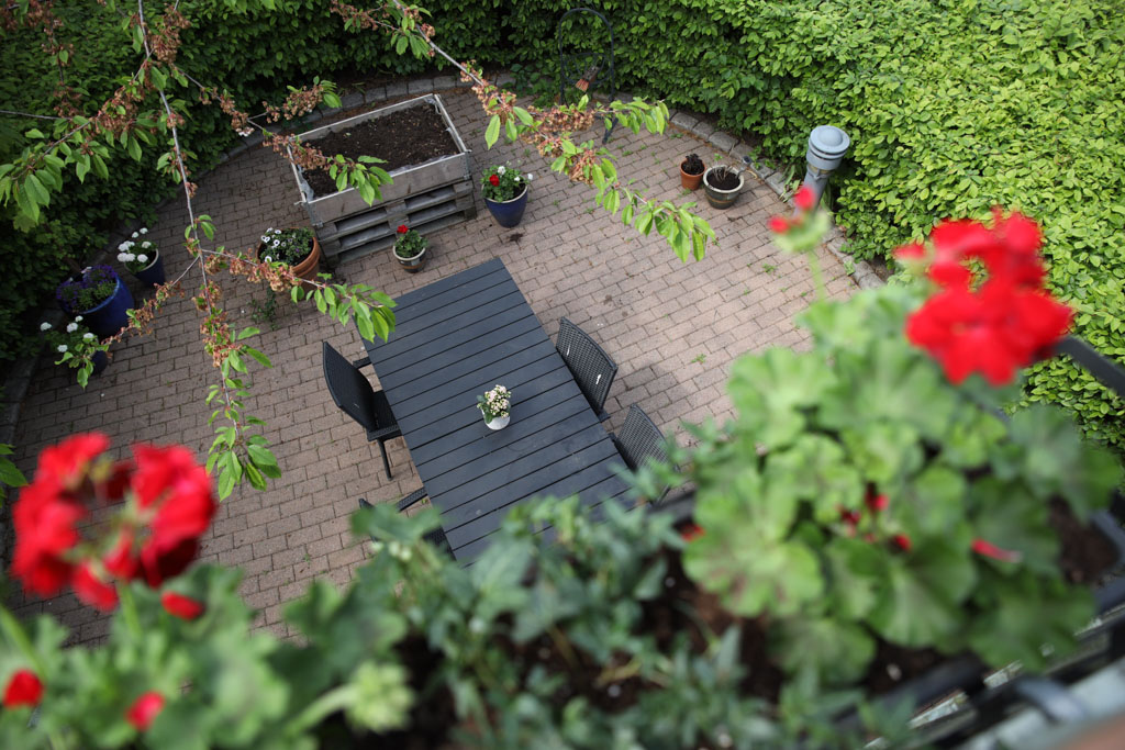 Från balkongen kan man se uteplatsen nedanför som är omringad av gröna buskar.