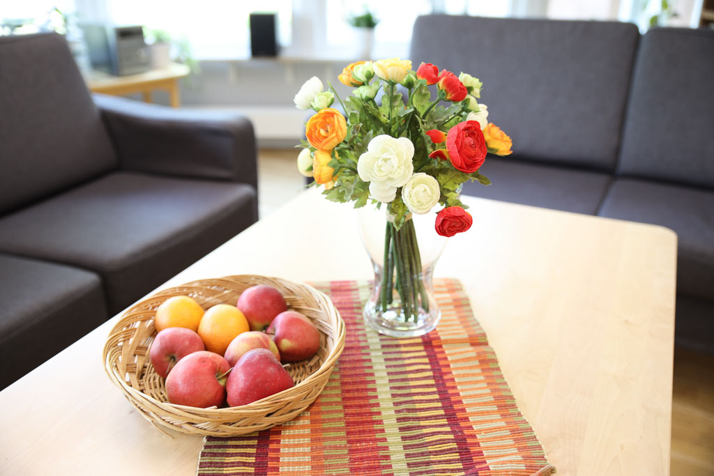 En fruktskål på bordet samt en färgglad bukett med blommor i en vas gör sällskapsrummet mer trivsamt.