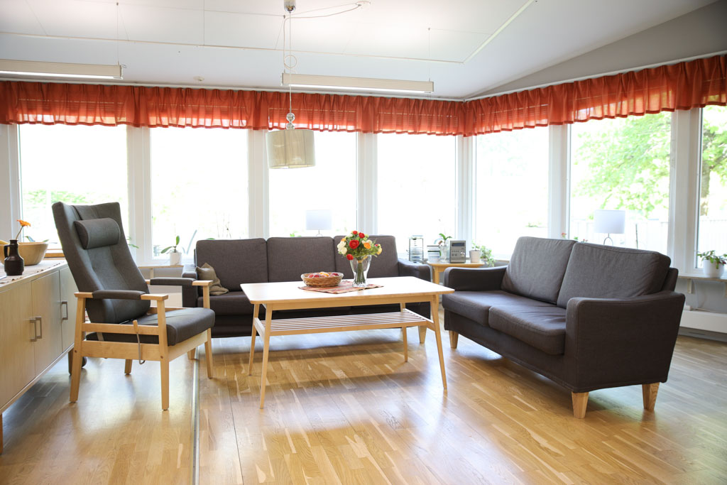 Sällskapsrummet med soffgrupp och fåtölj är omringat av fönster för stort ljusinsläpp.