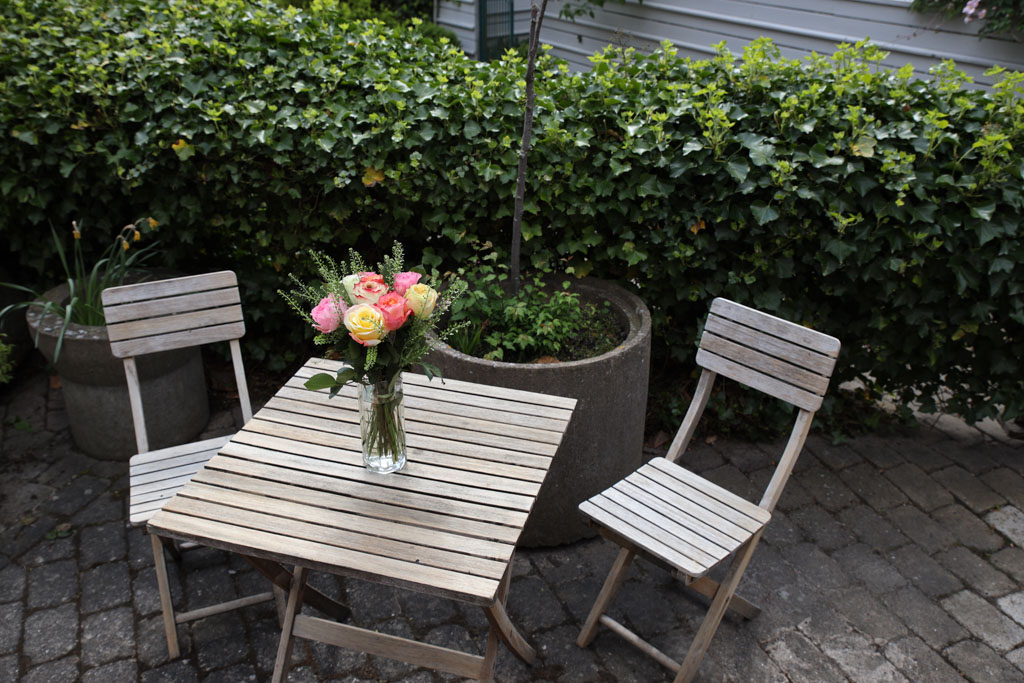 Vid ett tvåmannabord på uteplatsen kan man umgås med en vän, omringad av gröna buskar.