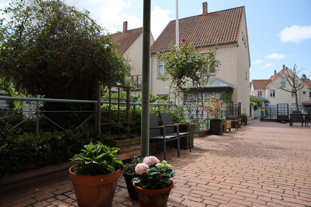 Den stora stenlagda uteplatsen är omringad av grön växtlighet. Här finns plats för umgänge i skyddad miljö.