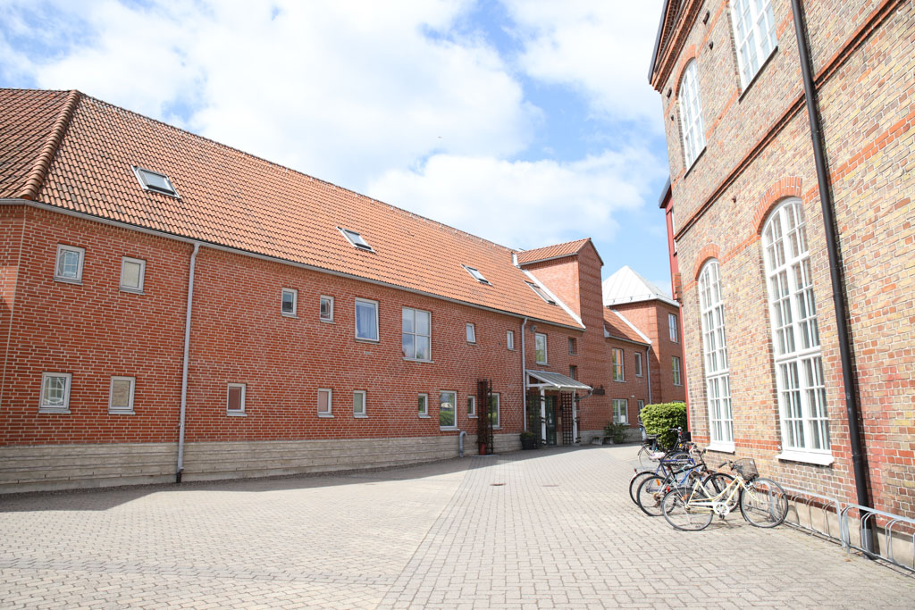 Ett tegelhus på en öppen och lugn gata välkomnar den besökande in. Huset har utsikt över ett gammalt vackert hus med höga fönster.