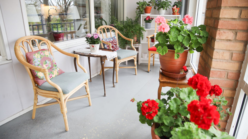 Den inglasade balkongen har ett härligt ljusinsläpp. Stolarna har färgglada kuddar och i krukorna står röda och rosa pelargonier.