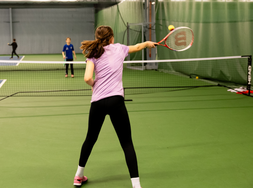 Ung person spelar tennis med ryggen vänd mot kameran