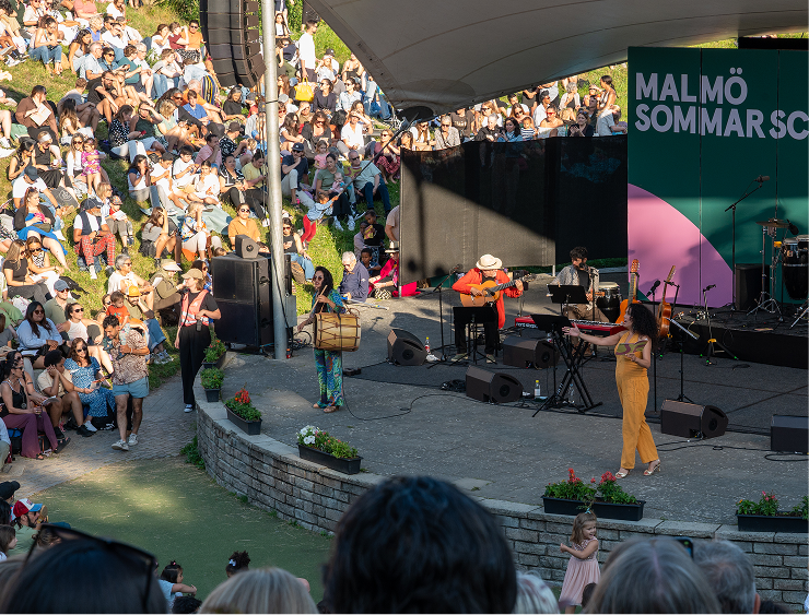 Sommarkväll på Pildammsteatern i varmt ljus. Festlig stämning, artister, ballonger och massor av publik.