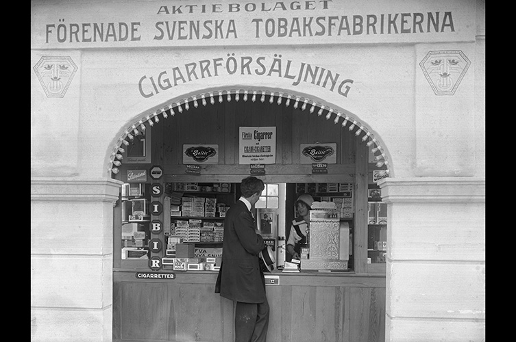 Äldre fotografi på man som står framför en byggnad med texten cigarrförsäljning