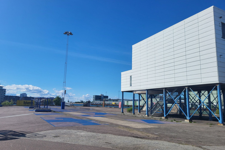 Industriområde vid hamnen, mitt i bilden ett flertal nybyggda blå bänkar av återvinningsmaterial.