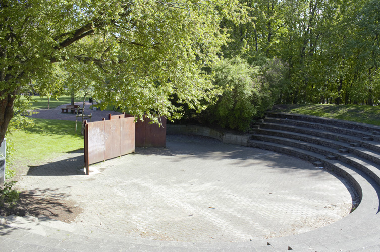 Stor öppen gräsmatta i en park, i bakgrunden flerfamiljshus.