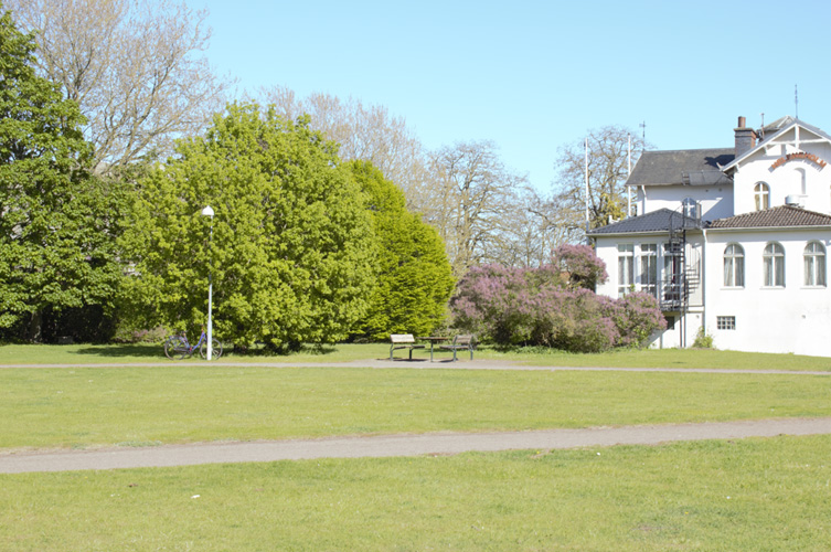 Liten park med vit herrgårdsliknande byggnad.