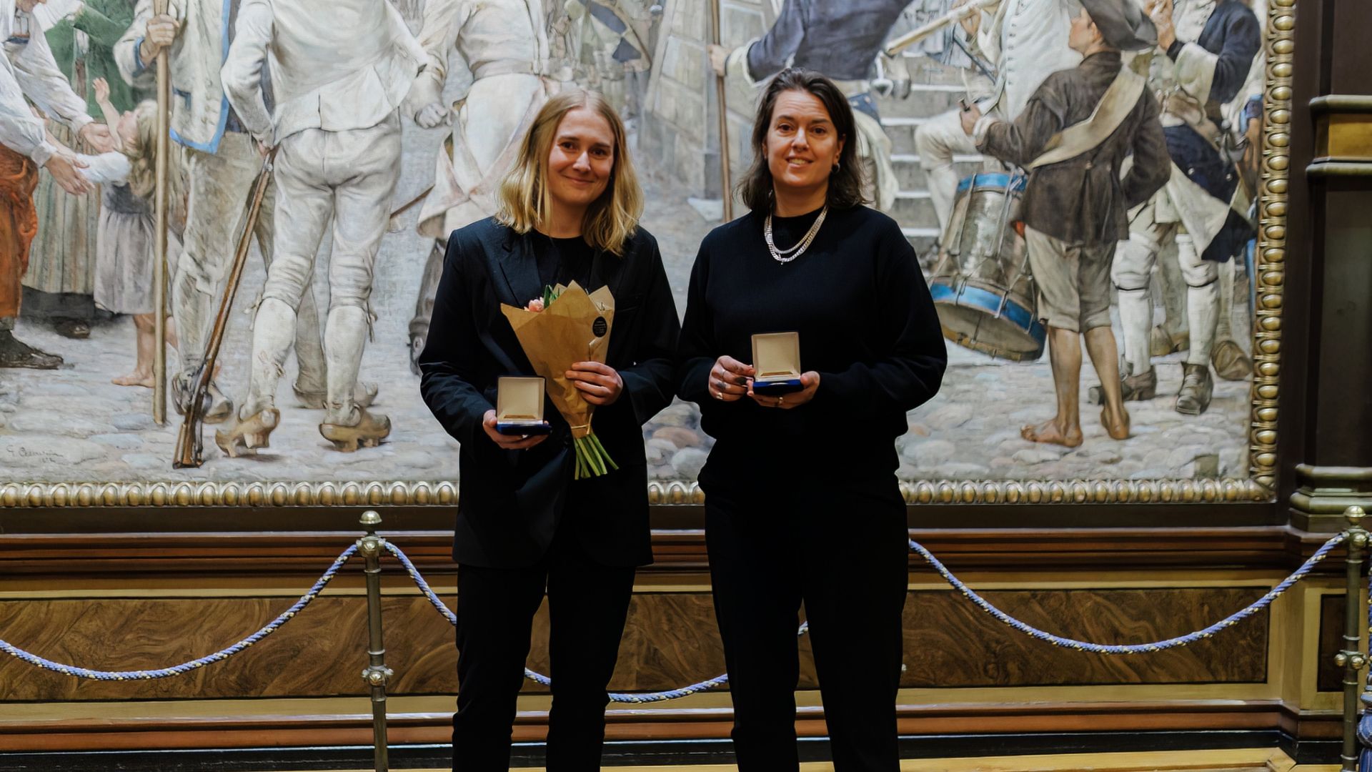 Klara Thell Lenntorp och Anna Oehme står tillsammans på scenen och håller upp sina medaljer.