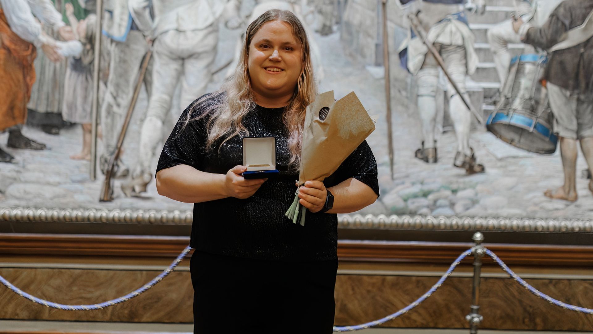 Matilda Hjäll ler glatt och håller upp sin medalj och blommor.