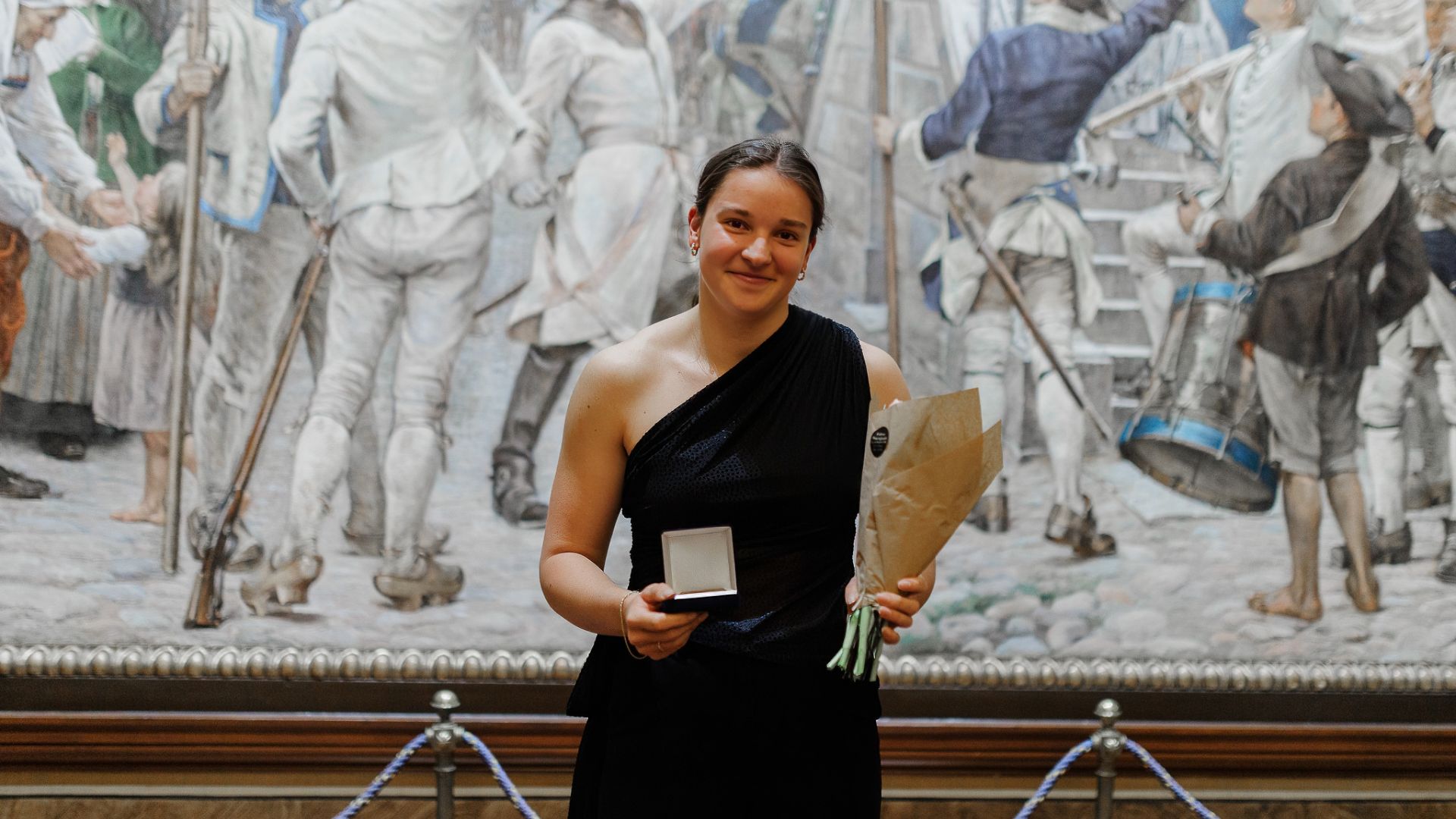 Ella Richter i en elegant klänning håller upp sin medalj och blommor.