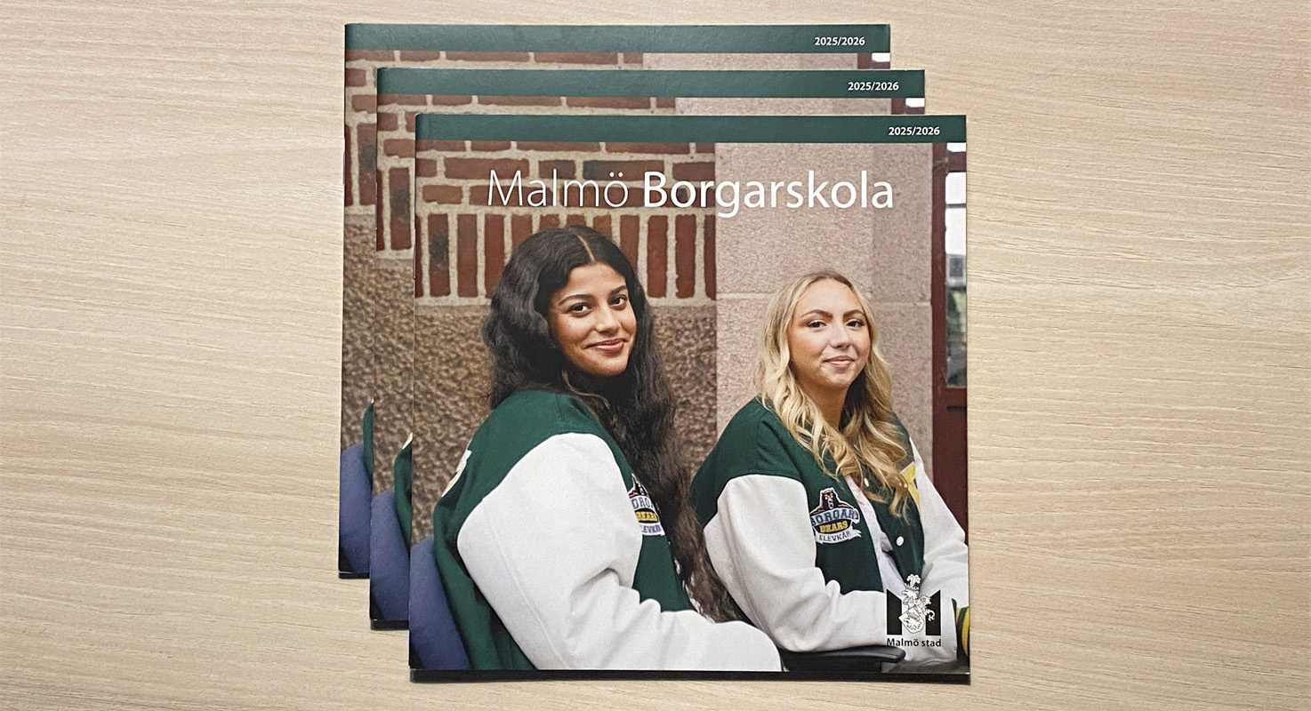 Tre exemplar på en tryckt katalog ligger staplade på en ljusfärgad yta. På katalogens omslag syns två glada elever iklädda grönvita varsityjackor.