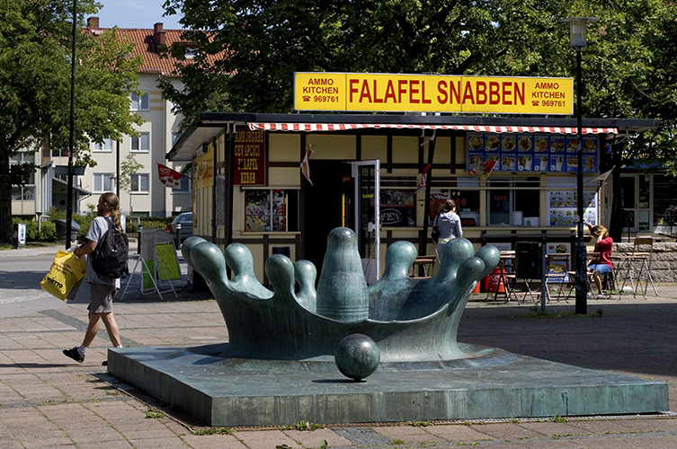 Ett torg med en ärgad fontän i form av en kungakrona framför en falafelkiosk.