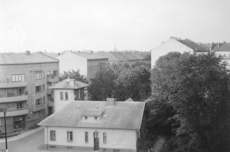 Svartvitt foto på en ljus villa intill en gata. På andra sidan gatan finns fyrvåningshus.