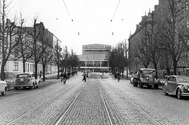 Trädkantad paradgata som leder upp mot stor byggnad. Svartvitt foto.
