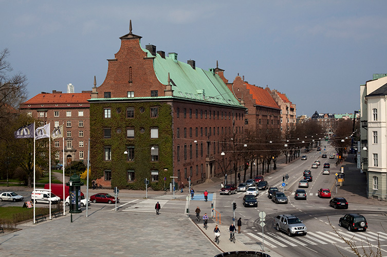 Stor röd pampig byggnad vid vägkorsning. Foto.