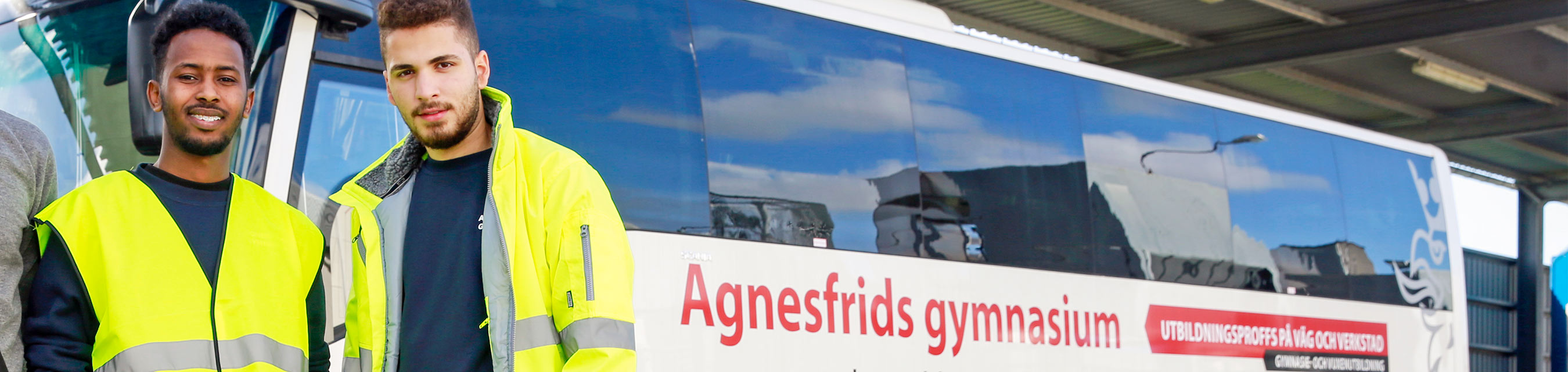 Två elever i varselkläder uppställda framför Agnesfrids gymnasiums övningsbuss. 