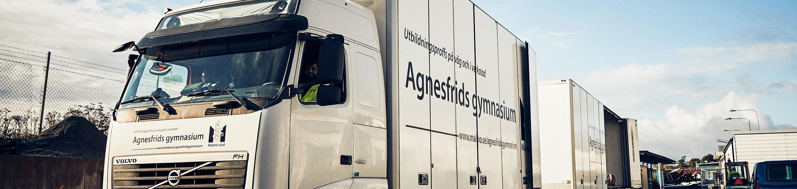 Skinande ren lastbil blänker i solen en frisk höstdag. På lastbilens skåp står det Agnesfrids gymnasium med stora svarta bokstäver. 