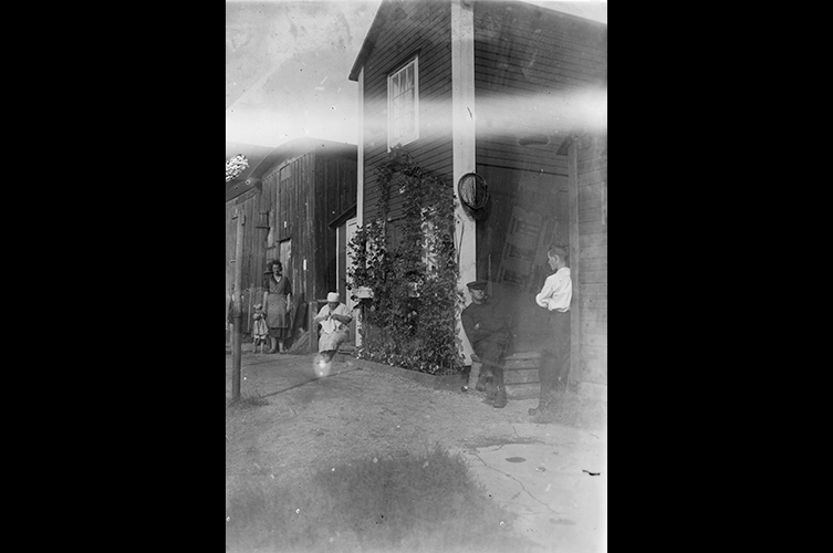 Små trähus/bodar med några människor i bild. Svartvitt foto.