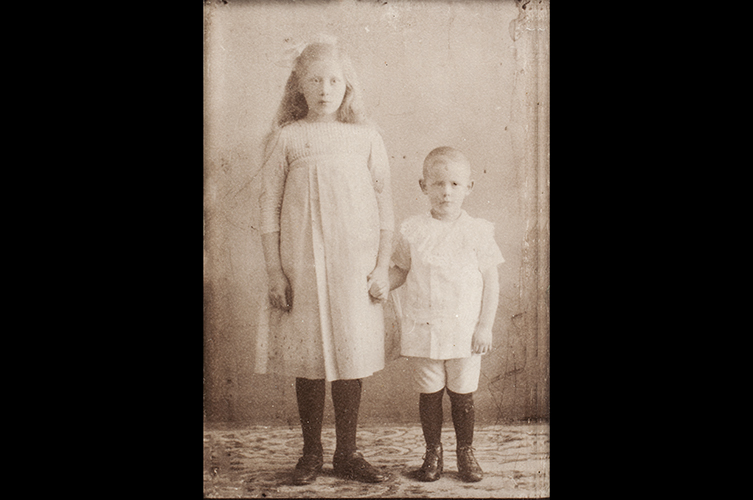 Äldre fotografi, på bilden står två barn i vita kläder och mörka strumpor.