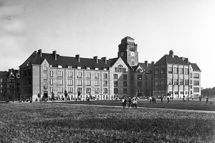 Äldre fotografi på Johannesskolan, en stor byggnad i tegel. Framför skolan finns en stor gräsmatta. 