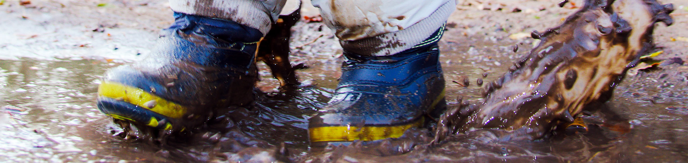 Ett barn iförd stövlar och overall leker i en vattenpöl.
