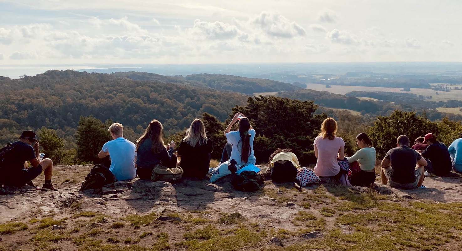 En grupp elever, sett bakifrån, sitter utspridda längs en klippa och blickar bort mot horizonten.