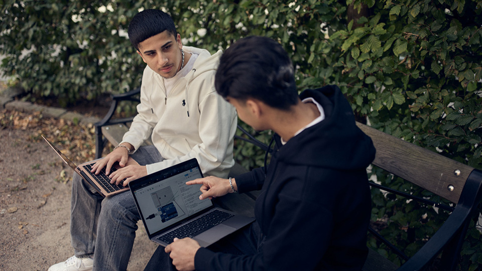 Två elever på IT-programmet sitter på en bänk på skolgården och programmerar.