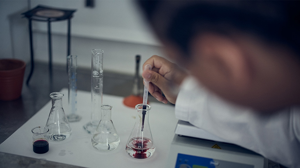 En elev gör en biologilaboration. Närbild på hand, pipett och labbglas.