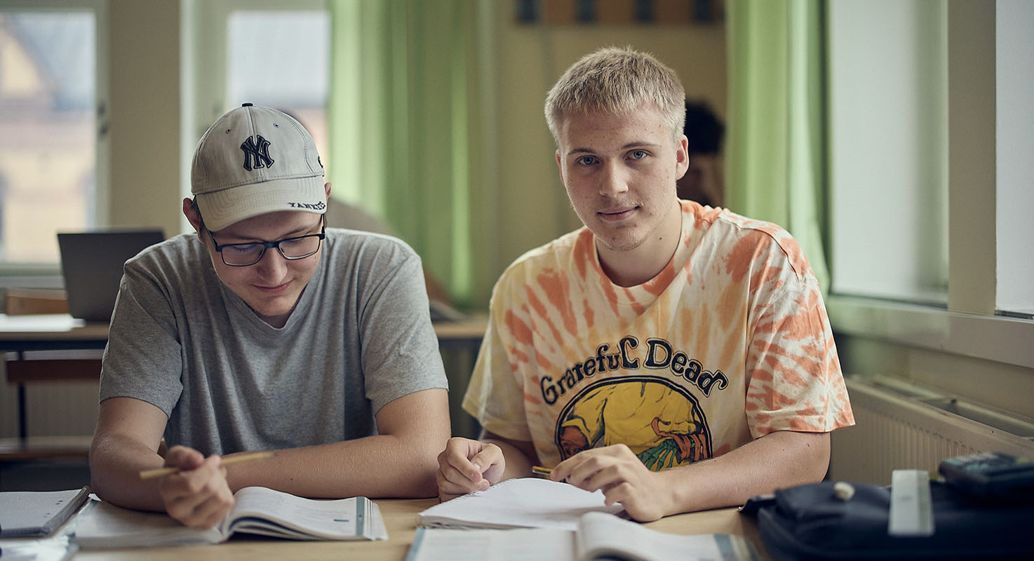 Två elever sitter bredvid varandra vid ett bord i ett klassrum och räknar matematik. 