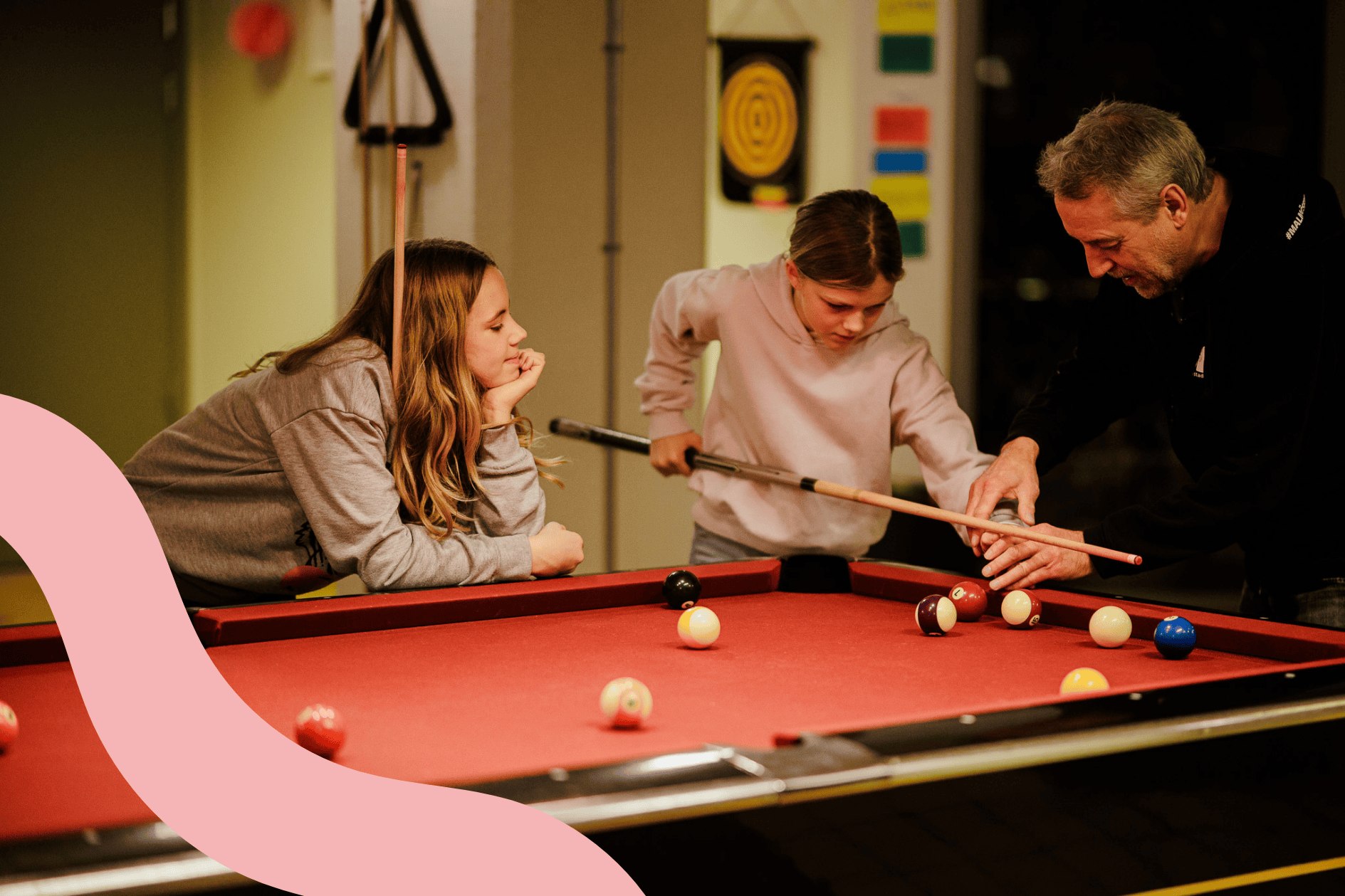 Ungdomar spelar biljard och får hjälp av en fritidsledare.