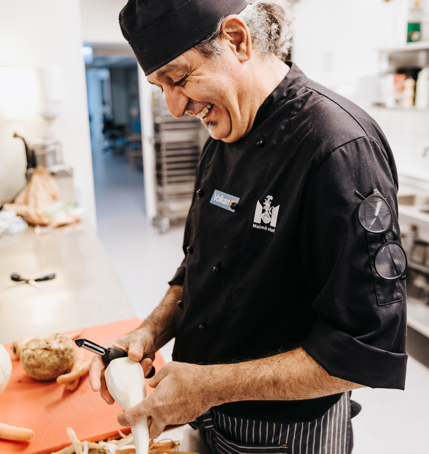 Man i svart klädsel skalar en palsternacka. Han ler stort.