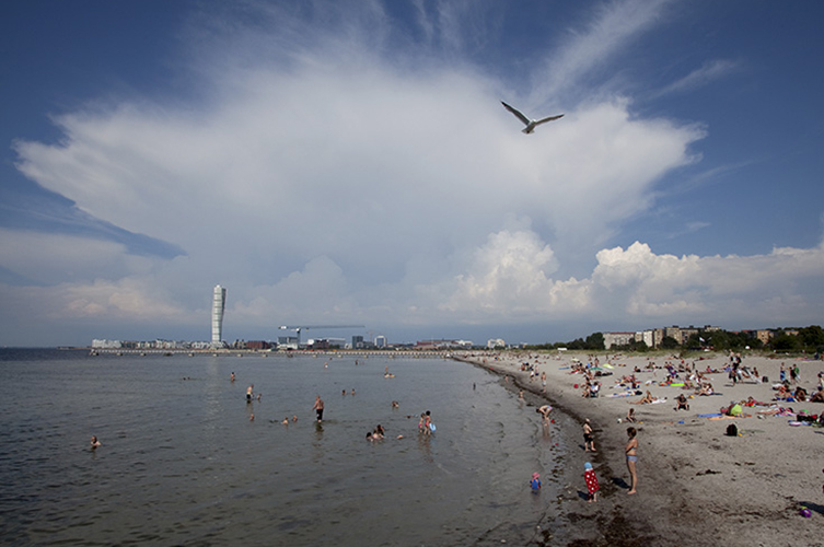 Strand med många badgäster. Ensam skyskrapa i bakgrunden. 