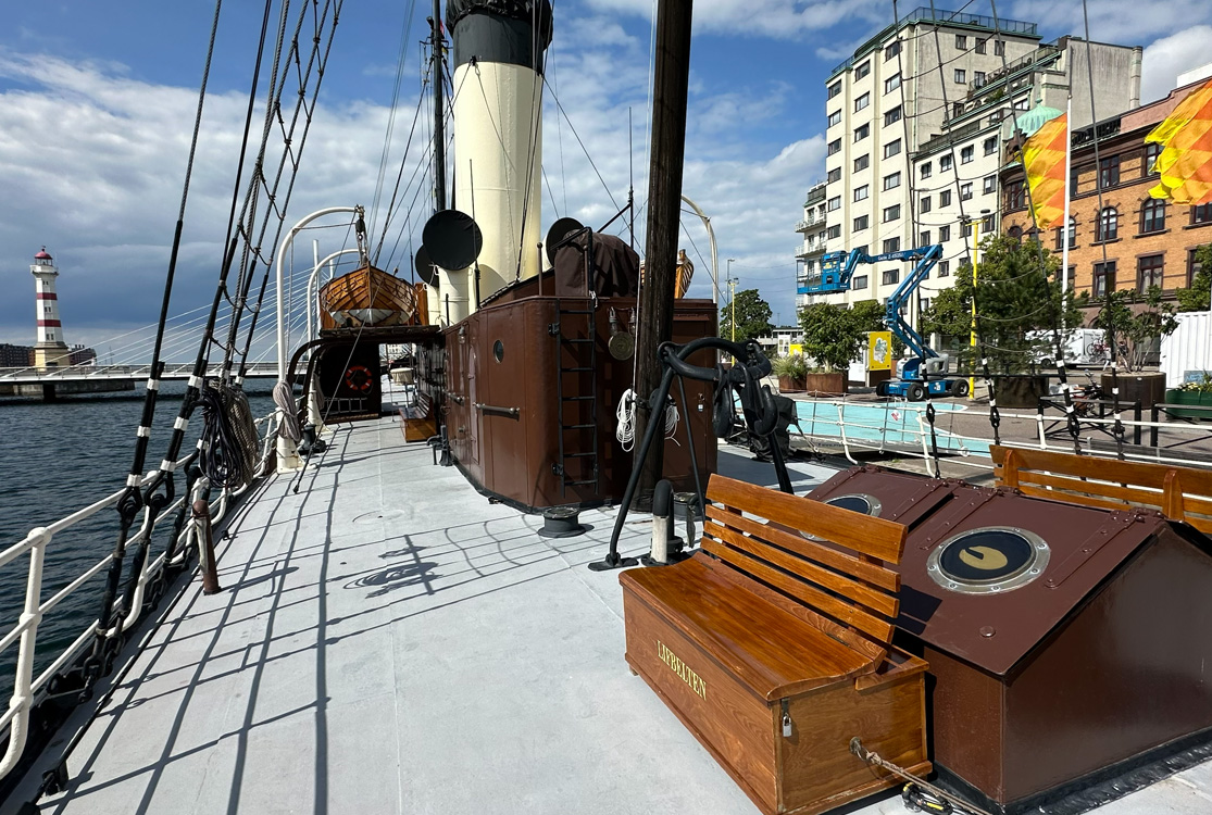 Däcket på en äldre båt med en vit och svart skorsten.