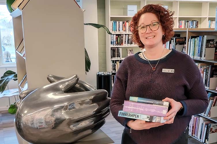 Jessica visar upp sina tre boktips inne på Husiebiblioteket.