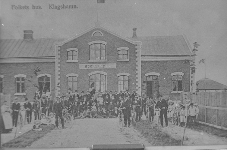 Äldre svartvitt fotografi med äldre byggnad med en stor folksamling framför.