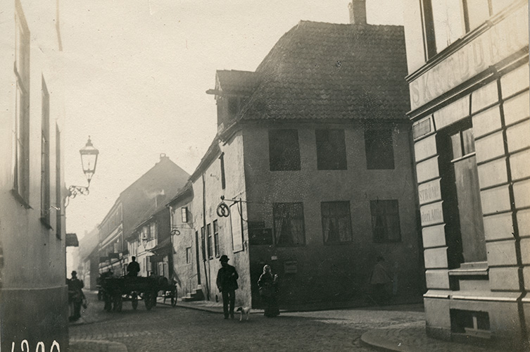Äldre svartvit foto av korsningen. Ett ekipage med häst och vagn kör förbil. Två våningar höga hus på hela gatan.