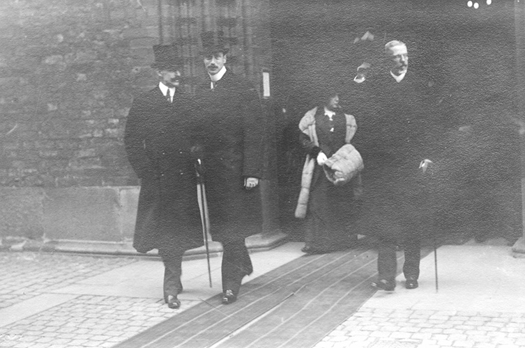 Svartvitt foto av Håkon och Christian tillsammans med Gustav V framför byggnad.