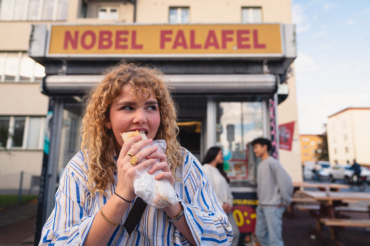 Tjej äter falafel framför kiosk