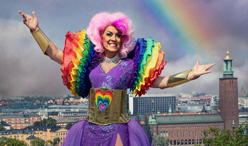Babsan har rosa hår, är klädd i en lila balklänning och står med en vy av Stockholm i bakgrunden.