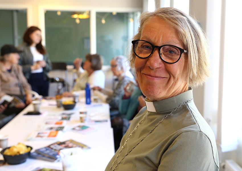 Ilse har ljust hår i en page, svarta glasögon och en klädsel med prästkrage.