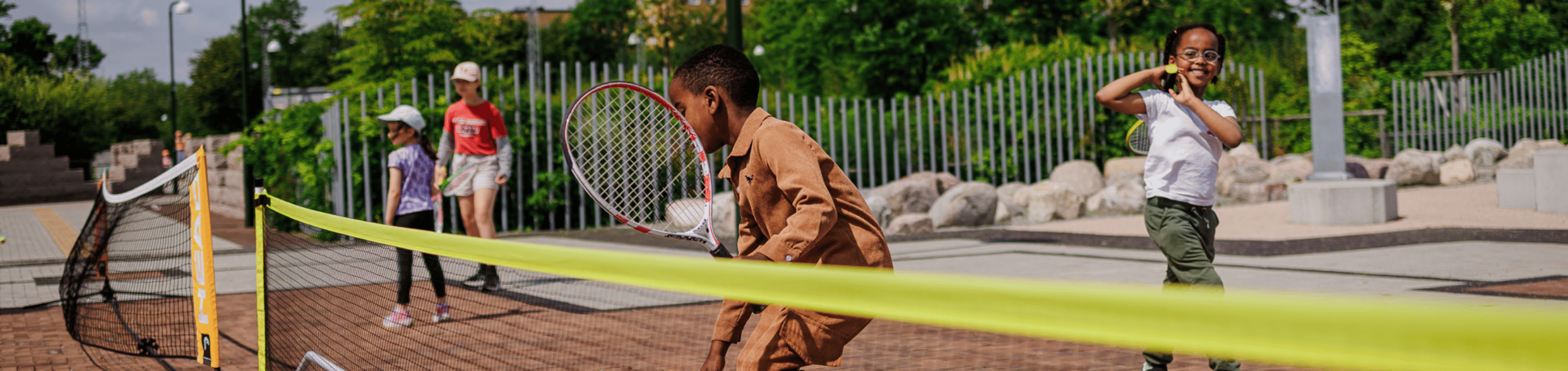 Barn spelar tennis utomhus.