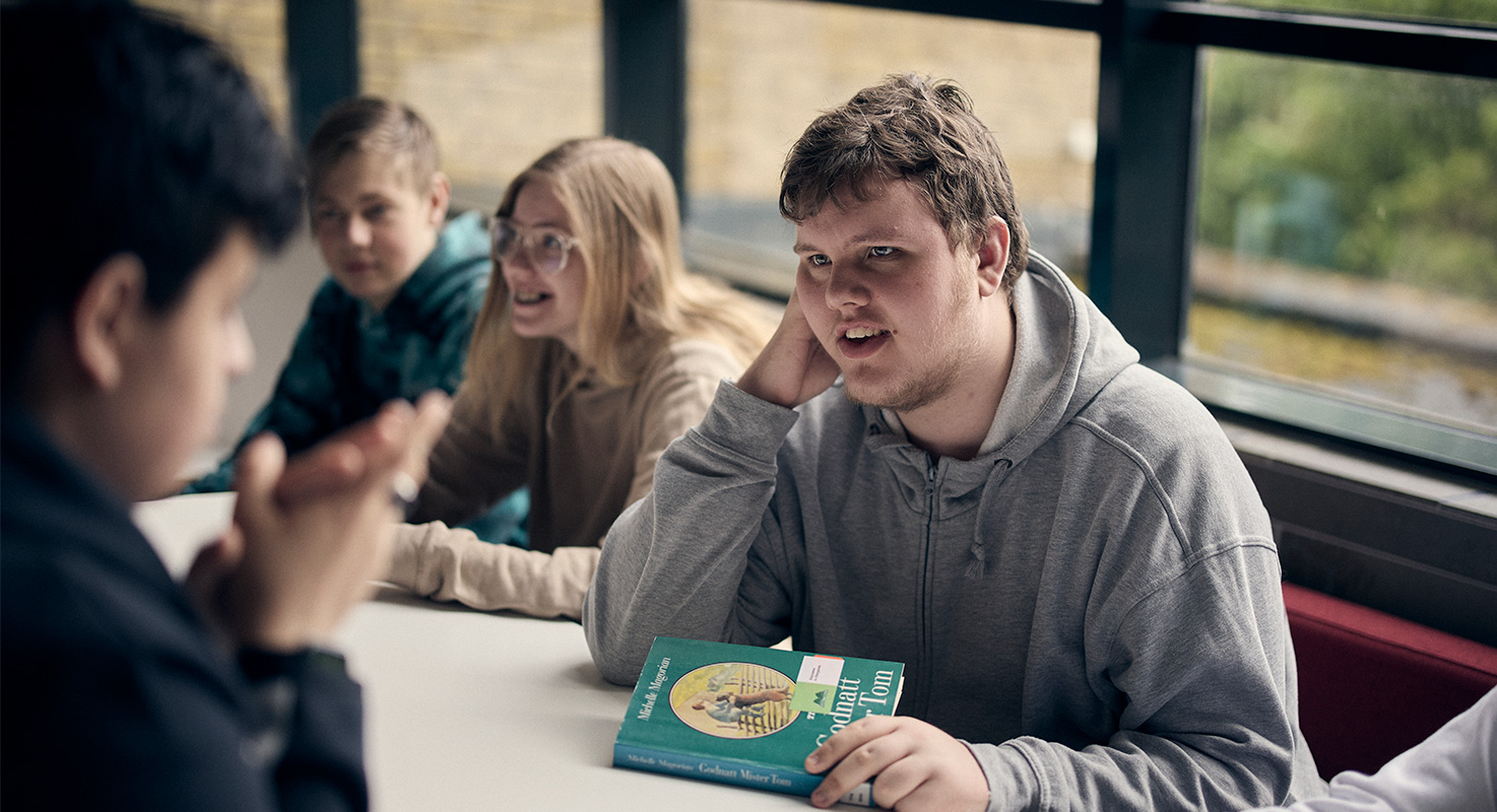 Elever i grupp sitter och pratar tillsammans. En av eleverna håller i en bok.