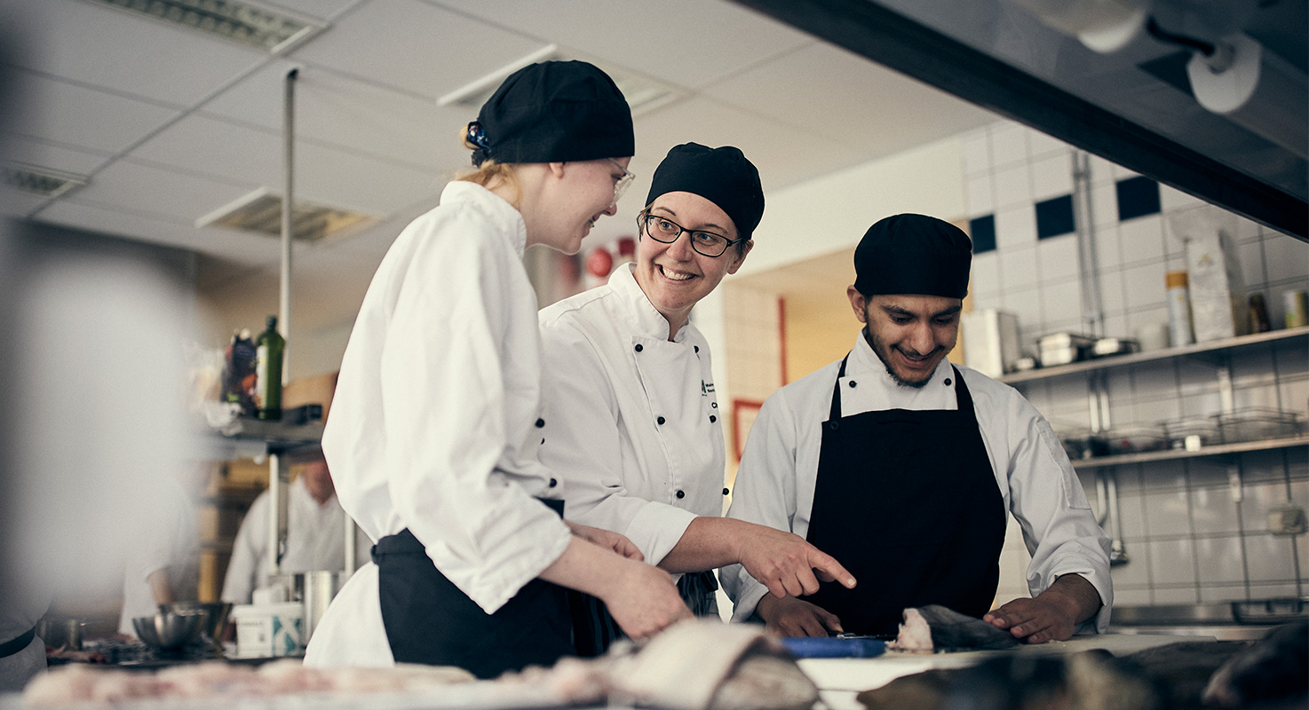 Lärare i restaurangköket i dialog om styckning av fisk med två elever.