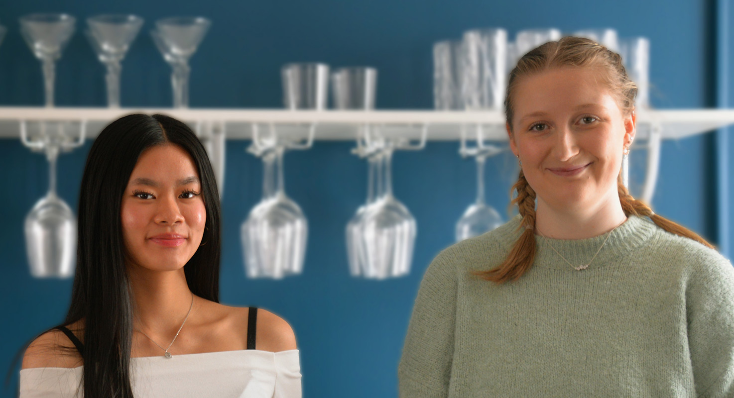 Fiona och Livia framför en hylla med vinglas.