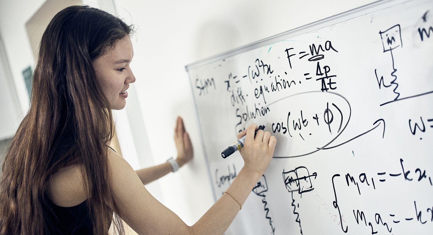 En elev löser matematiska problem på en whiteboardtavla.