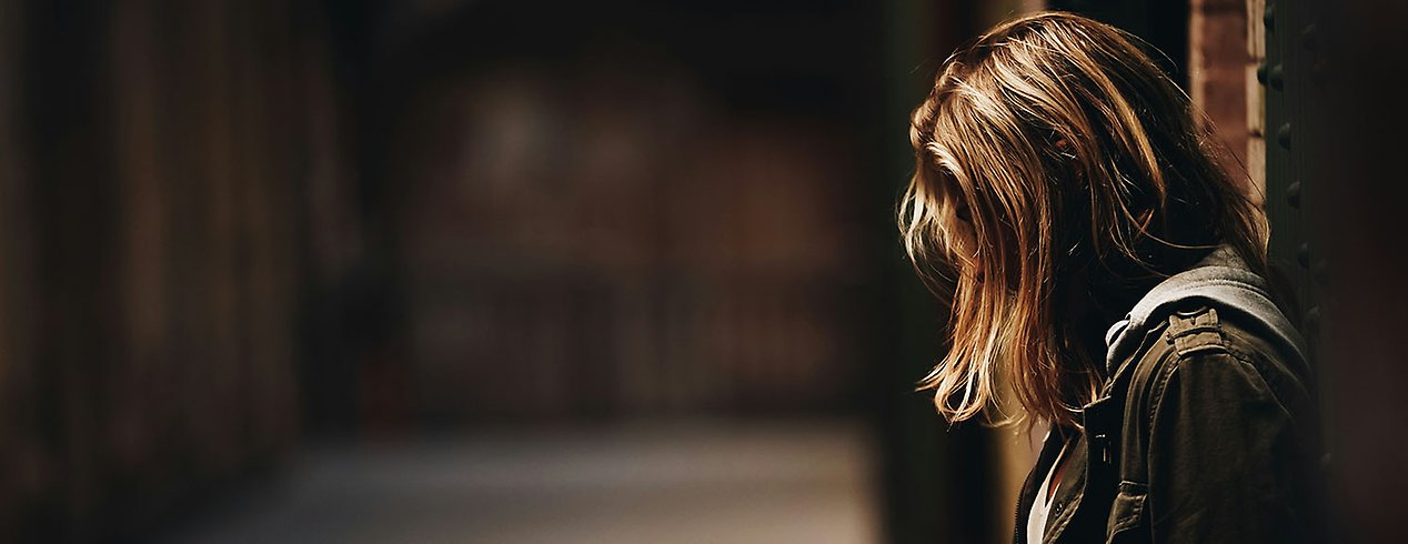 Ensam ung kvinna i profil står och tittar ner i marken.