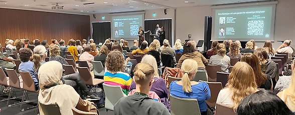 Från Mr-konferensen. Publik som tittar på tre personer på scenen.