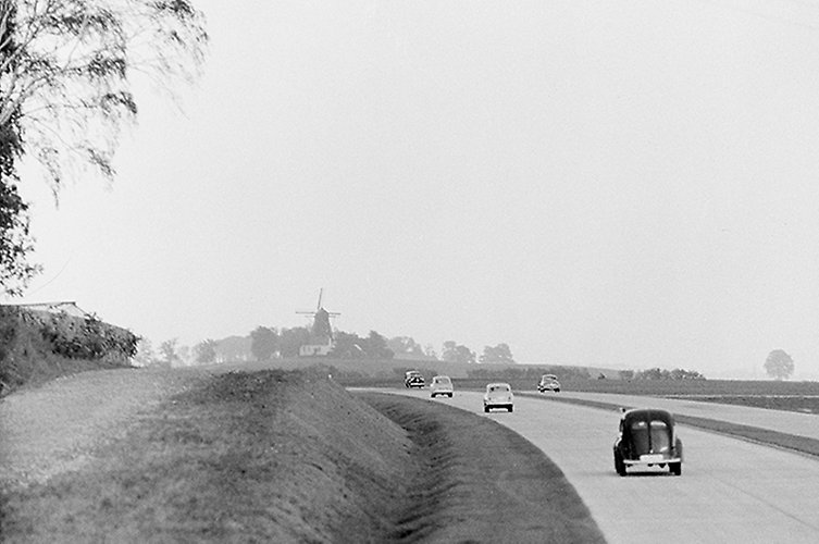 Svartvitt foto av landskap med vägren och motorväg. I bakgrunden syns en mölla.